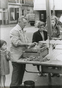 875242 Portret van Piet Schoonhoven ('Piet 't Joodje') die haringen schoonmaakt op zijn viskar op de hoek van de ...